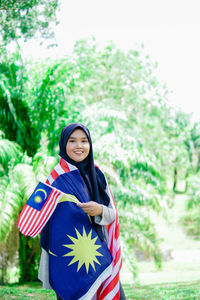 Portrait of young woman standing against trees