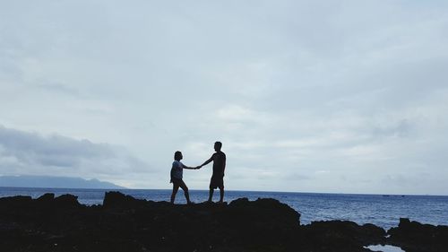 Man and woman standing on rock formation by sea against sky