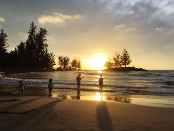 Silhouette people playing on beach against sky during sunset