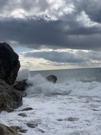 Sea waves splashing on rocks against sky