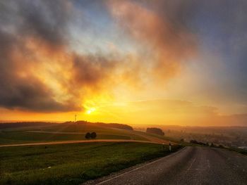 Road amidst field against sky during sunset