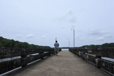Man sitting on bridge over river against sky