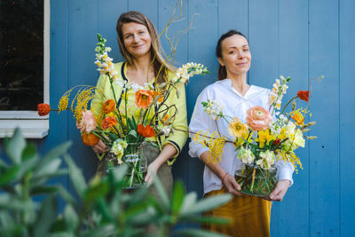 Two young women with beautiful bouquets of peonies in glass vases against the blue background