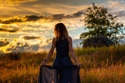 Rear view of woman standing on field against sky during sunset