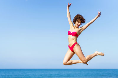 Full length of woman doing yoga at beach against clear sky