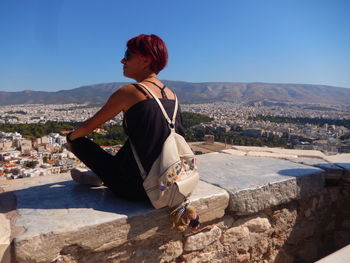 Woman sitting on retaining wall against sky