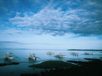 Outrigger boats moored in sea against cloudy sky