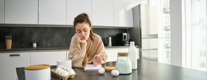 Side view of young woman sitting on table at home