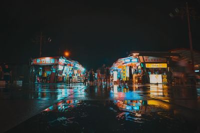 Illuminated buildings by wet street at night