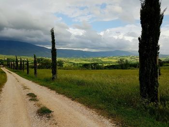 Road passing through field against cloudy sky