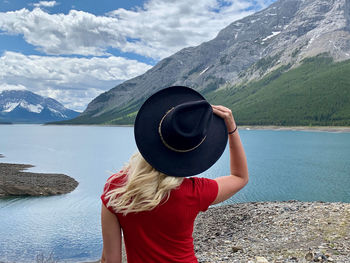 Rear view of woman standing by lake against mountains