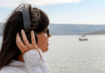 Beautiful young woman standing on beach listening to music on headphones.