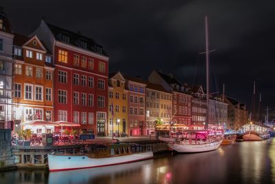 Boats moored on canal against sky in city at night