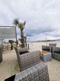 Chairs on beach against cloudy sky