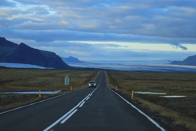 Road along field against cloudy sky during sunset