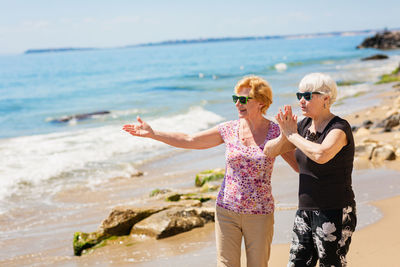 Two senior women are walking along the rocky shore, talking and laughing