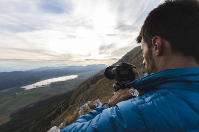 Rear view of man photographing mountains against sky