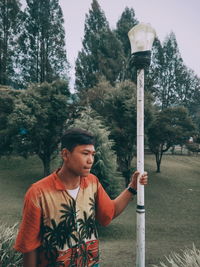 Portrait of young man looking away while standing against trees