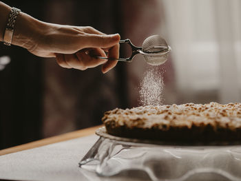 Close-up of hand sprinkling sugar powder on cake at table