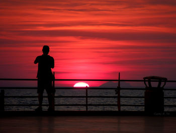 Silhouette man overlooking calm sea at sunset