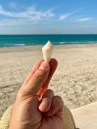 Midsection of hand holding ice cream on beach