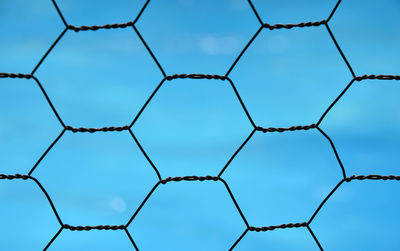 Full frame image of metallic fence against blue sky