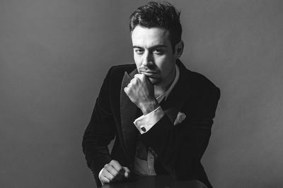 Portrait of young man sitting against gray background