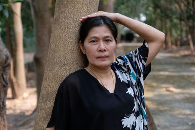 Portrait of mature woman against tree trunk in forest