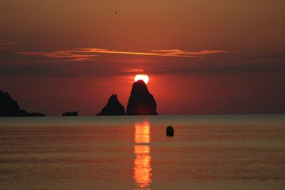 Silhouette rock in sea against sky during sunset