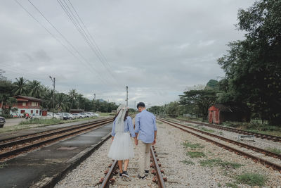 Rear view of man on railroad tracks against sky