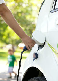 Cropped hand of person charging white electric car