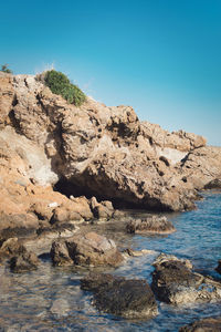 Rock formations on shore against clear blue sky