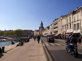 People on street amidst buildings in city against sky