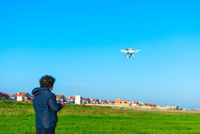 Boy looking at drone against clear blue sky