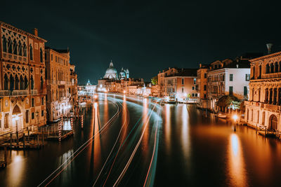 Light trails on river amidst illuminated buildings in city at night