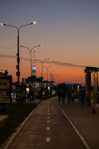 People walking on road against sky during sunset