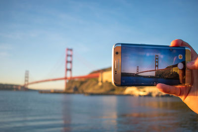 Close-up of hand holding mobile phone against river