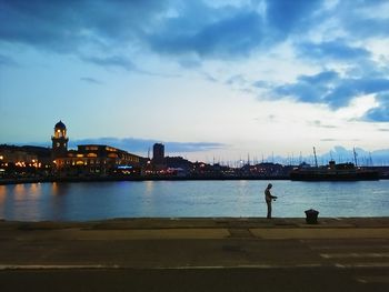 View of city at waterfront against cloudy sky