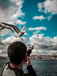 Rear view of man feeding seagull against sky