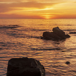 Rock formation in sea against sky during sunset