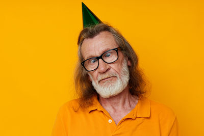 Senior man wearing party hat against yellow background