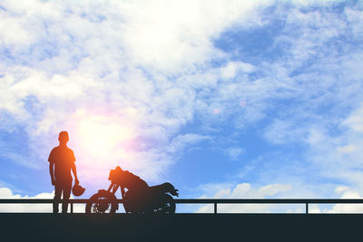 Silhouette people sitting on railing against sky