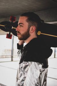 Side view of young man holding skateboard