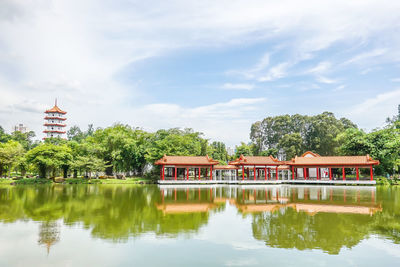 Reflection of building and trees by lake against sky