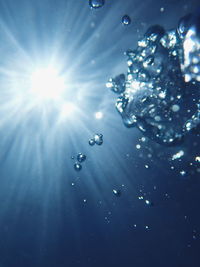 Low angle view of bubbles against blue sky on sunny day