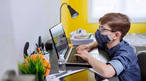 Boy wearing mask studying with laptop at home