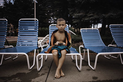 Portrait of boy sitting on lounge chair at poolside