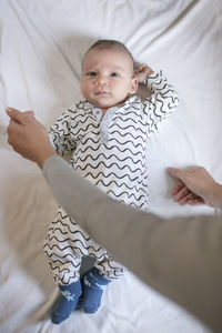 Cropped image of mother holding cute baby boy on bed at home