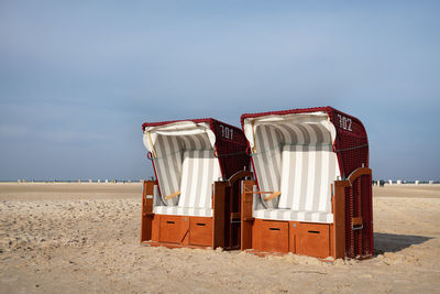 Hooded chairs on beach against sky