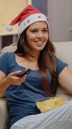 Smiling young woman eating snacks while sitting on sofa at home